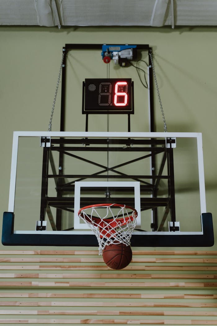 about-04 A basketball scoring through a hoop in an indoor court with scoreboard.